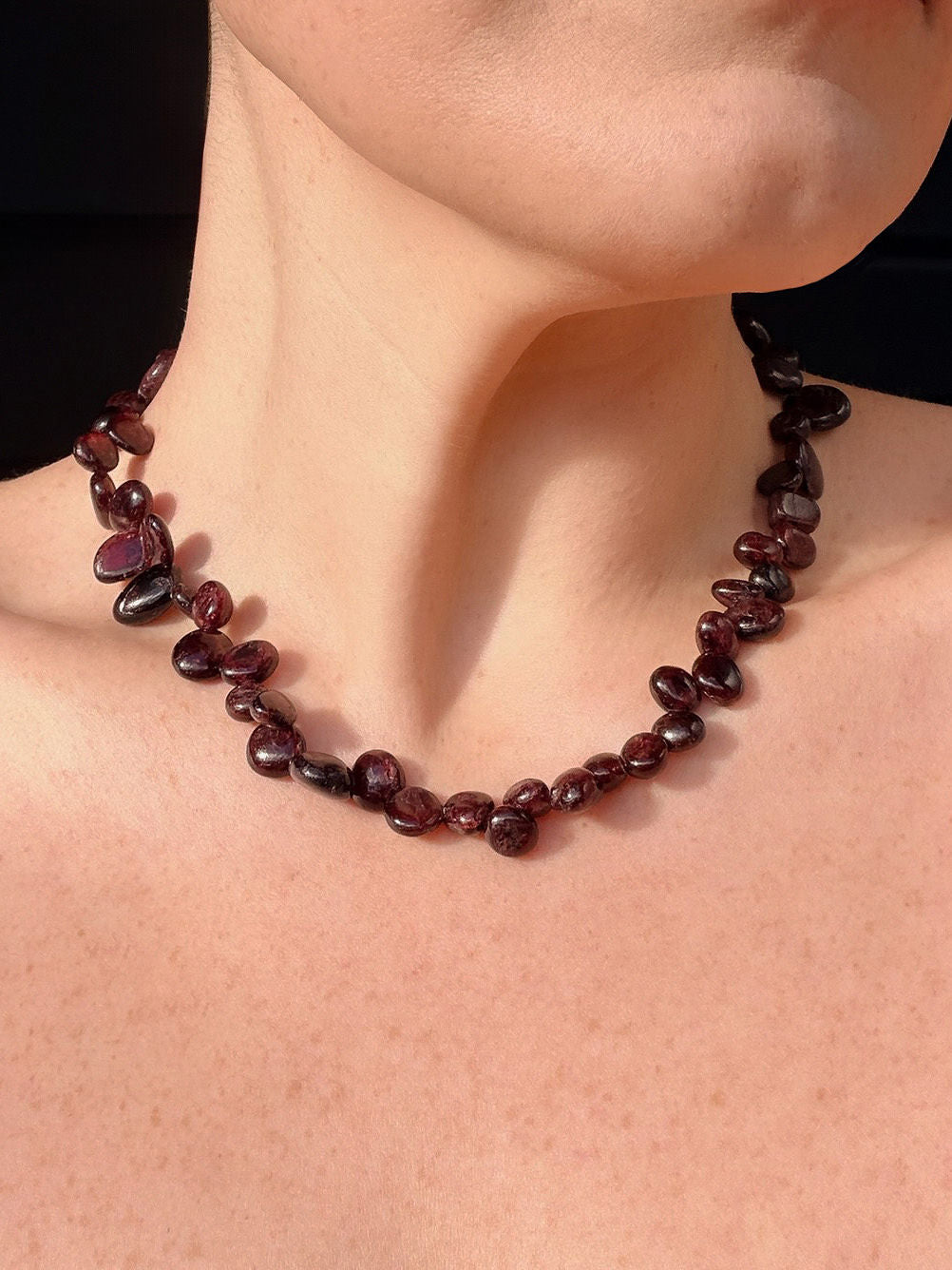 Garnet necklace on a person's neck with a black background